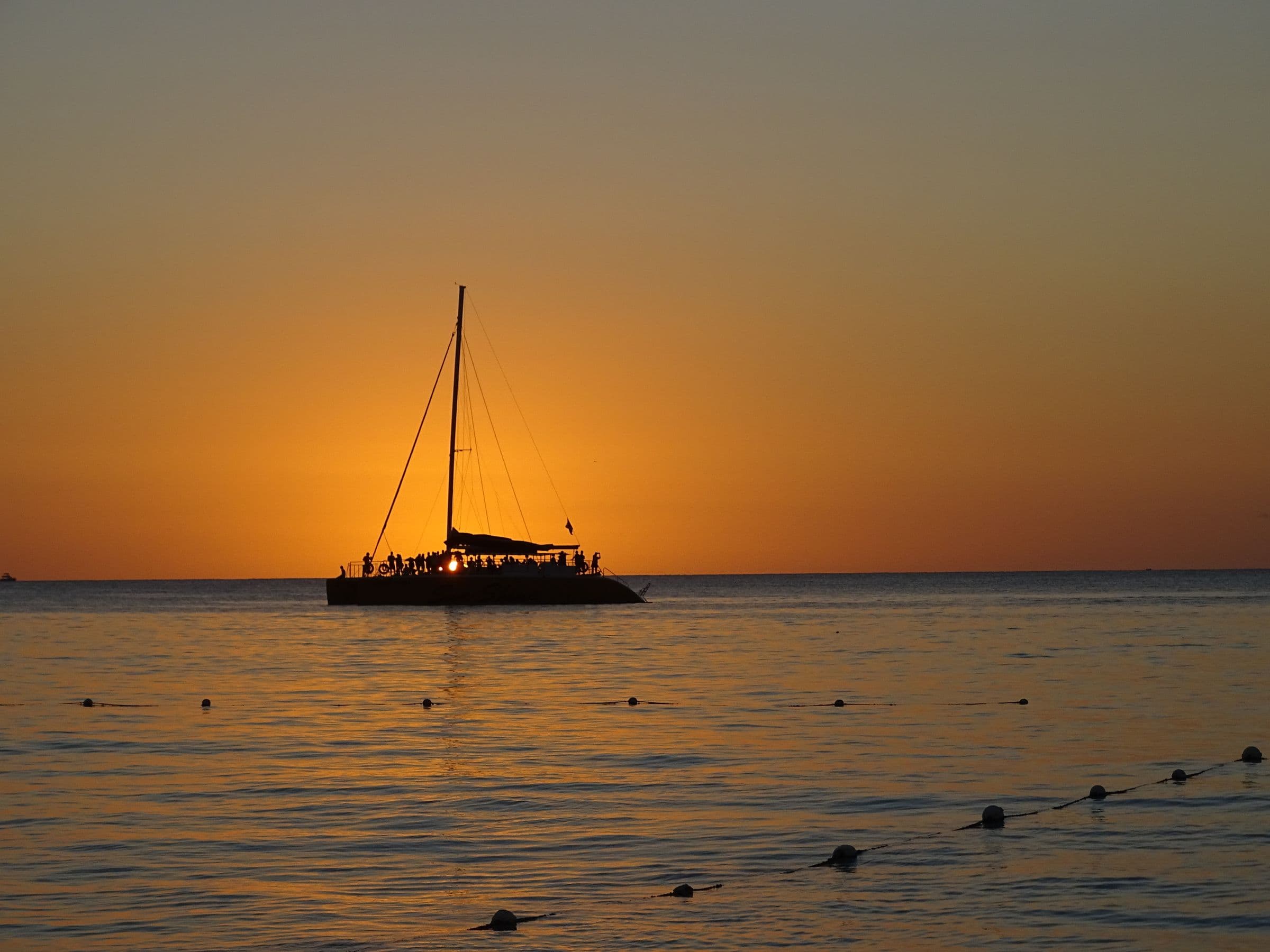 A catamaran silhouetted against an orange sunset over the sea off Negril, Jamaica