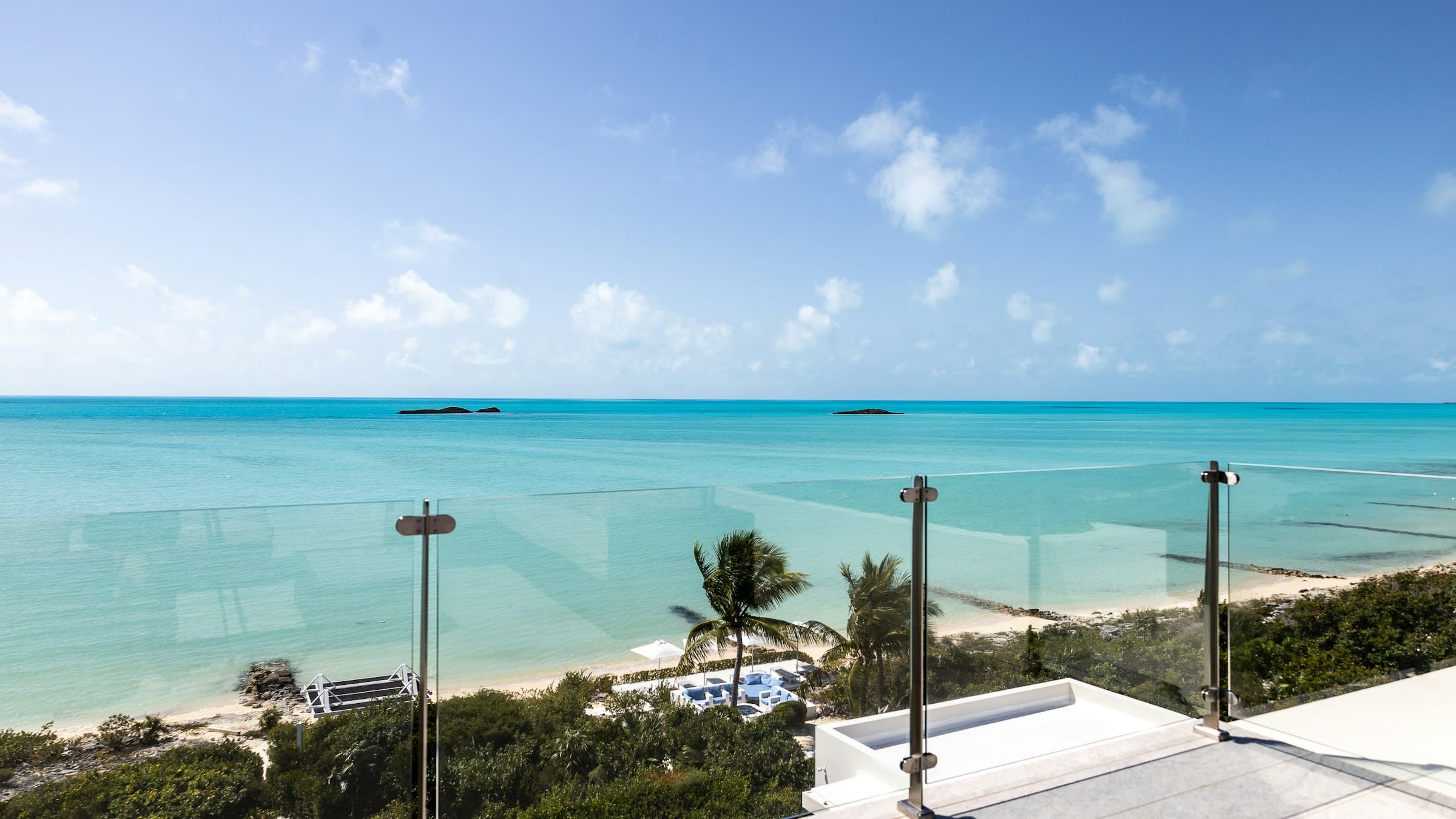 Illustrative image: glass balcony looking out over a turquoise bay and palm trees